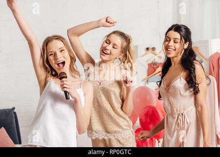 Beautiful smiling in multiethnique nightwear singing karaoke at soirée pyjama dans la chambre Banque D'Images