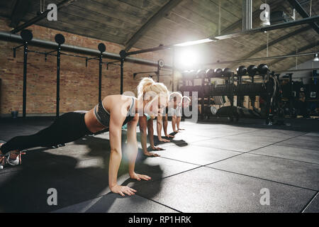 Groupe diversifié d'entrer les gens dans les vêtements de sport faisant pompes ensemble sur un plancher du gymnase lors d'une séance d'entraînement Banque D'Images
