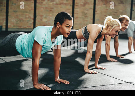 Groupe diversifié d'entrer les gens dans les vêtements de sport faisant pompes ensemble sur le plancher d'une salle de sport au cours d'une session d'entraînement Banque D'Images