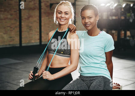 Deux jeunes amis féminins dans les vêtements de sport assis ensemble sur un fort à la salle de sport après une séance Banque D'Images