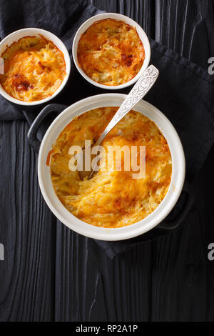 Gratin de pommes de terre cuite au four avec de la crème, des oignons et du fromage cheddar close-up dans une casserole sur la table. Haut Vertical Vue de dessus Banque D'Images