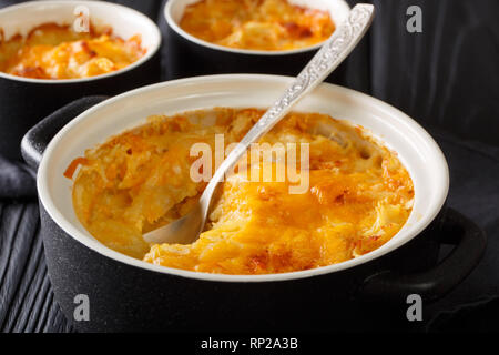 Gratin de pommes de terre cuite au four avec de la crème, des oignons et du fromage cheddar close-up dans une casserole sur la table horizontale. Banque D'Images