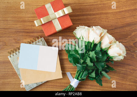 La Journée internationale des femmes concept. Carte de fleurs. Bouquet de roses, cadeau et carte vierge sur fond de bois. La Fête des mères. Vue de dessus Banque D'Images