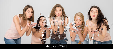 Happy girls blowing sur confetti étoile isolé sur gray Banque D'Images