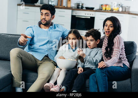 L'homme pointant avec le doigt tout en regardant la tv avec hispanic family at home Banque D'Images