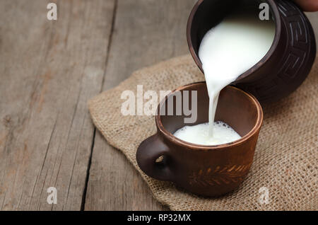 Verser le lait frais dans une tasse d'argile sur fond de bois. Banque D'Images