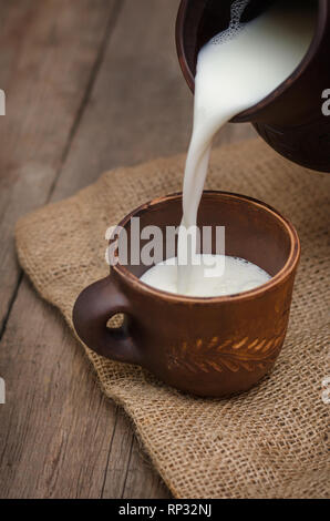 Verser le lait frais dans une tasse d'argile sur fond de bois. Banque D'Images