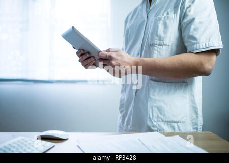 Médecin dans l'uniforme à l'aide de tablette de l'ordinateur à côté de son bureau à l'hôpital 24 Banque D'Images