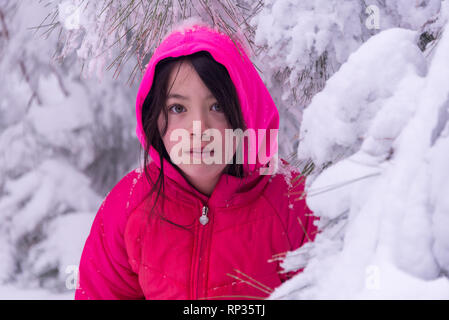 Jeune fille debout dans les arbres couverts de neige avec dossier rose Banque D'Images