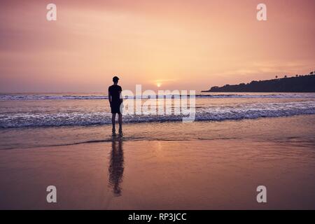 La contemplation pendant beau lever de soleil. Jeune homme sur la plage de sable idyllique près de Tangalle au Sri Lanka. Banque D'Images