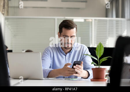 Office worker sitting in espace de coworking est titulaire téléphone mobile message d'affaires lecture ou surfer sur internet. Businessman typing millénaire communication Banque D'Images