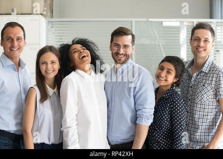 Plusieurs employés heureux millénaire ethnique permanent dans la rangée posing looking at camera. Six employés de bureau réussie sourire se sent motivé prêt à succ Banque D'Images