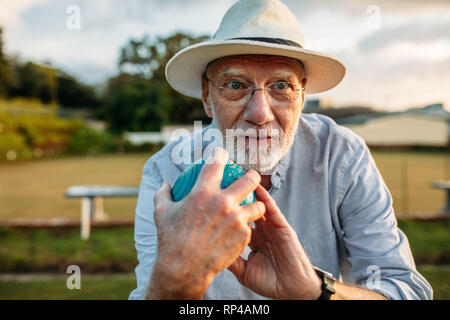 Monsieur âgé tenant une tranche dans la main prenant position pour lancer. Portrait d'un vieil homme en hat de jouer à un jeu de boules dans un parc. Banque D'Images