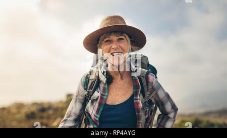 Cheerful woman sa randonnée standing outdoors. Portrait d'une femme portant un chapeau et sac à dos sur une vacances. Banque D'Images