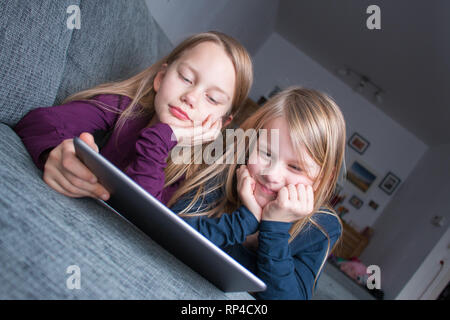 Les filles sont allongés sur un canapé et regarder quelque chose de drôle sur un ipad Banque D'Images