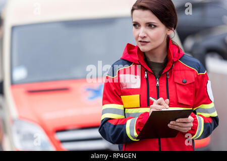 Female paramedic en uniforme rouge écrit dans le presse-papiers Banque D'Images