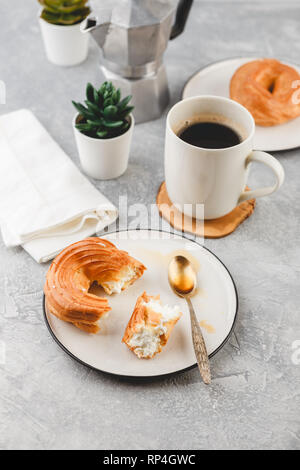 Le petit-déjeuner avec anneaux - chou à la crème, pâte à choux et tasse de café noir sur fond clair Banque D'Images