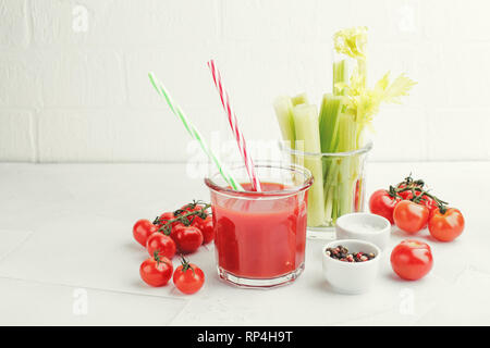 Verre de délicieux jus de tomate avec deux pailles à rayures, branches de céleri frais, sel, poivre et les tomates cerises juteuses fraîche sur un fond clair. B Banque D'Images