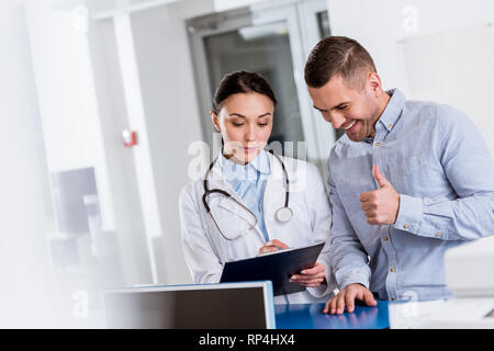 Showing thumb up patient médecin alors que l'écriture dans le presse-papiers Banque D'Images