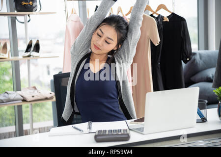 Creative designer asiatique s'étendant les bras et fermer les yeux devant l'ordinateur portable sur un bureau Banque D'Images