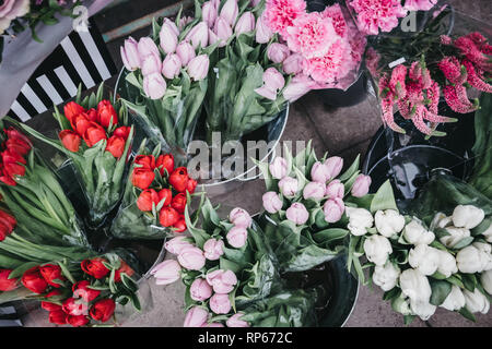 Grappes de fruits rouges, roses et tulipes blanches en vente sur un marché de rue. Banque D'Images