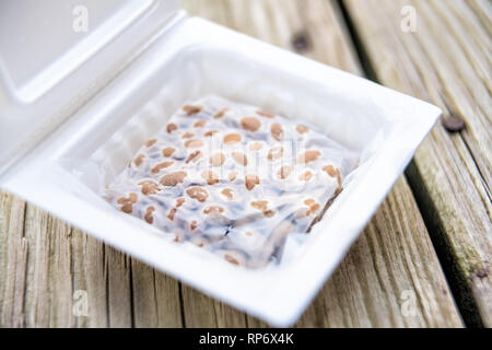 Gros plan du natto japonais asiatique plat de soja fermenté avec repas film papier couvercle en styrofoam container Japon fort sur macro table en bois Banque D'Images