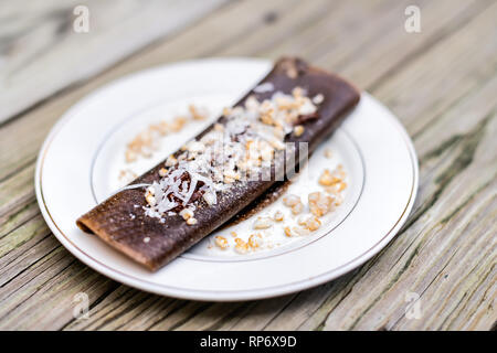 Gros plan du vegan chocolat dessert crêpe wrap avec du riz chips et flocons de noix de coco faite en bouteille avec des bananes sur la plaque de table en bois Banque D'Images