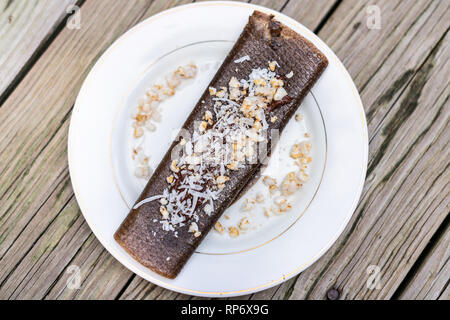 Gros plan dessus plat de crêpes au chocolat dessert wrap avec du riz chips et flocons de noix de coco faite en bouteille avec des bananes sur la plaque de table en bois Banque D'Images