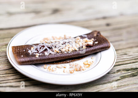 Gros plan du wrap crêpes au chocolat avec du riz chips et flocons de noix de coco faite en bouteille avec banane dessert sur assiette table en bois Banque D'Images