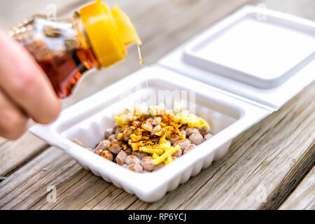 Le natto japonais asiatique plat de soja fermenté contenant en styromousse repas au Japon fort libre et versez de l'huile de sésame grillées sur l'ail et le gingembre sur sol en bois Banque D'Images
