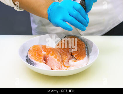 Chef putting sel sur la tranche de saumon, recadré de mains cuisine poisson Saumon Banque D'Images