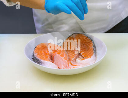 Chef putting sel sur la tranche de saumon, recadré de mains cuisine poisson Saumon Banque D'Images