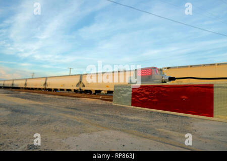 Close-up de la fin pointe d'une barrière de fer à un niveau de la rampe de passage à niveau avec un train passant par en arrière-plan ; Bryan, Texas, USA. Banque D'Images