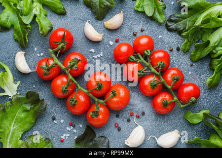 Tomates cerises sur une branche d'herbes fraîches et gousse d'ail avec les épices sur une table en pierre Banque D'Images