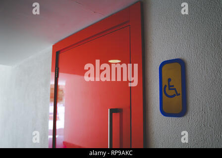 Une entrée aux toilettes pour handicapés. Badge. Vue d'une rouge porte des toilettes avec mobilité panneau sur la droite sur le côté. Banque D'Images