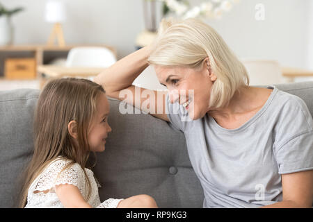 Petite-fille de parler avec grand-mère attentive, sitting on sofa Banque D'Images