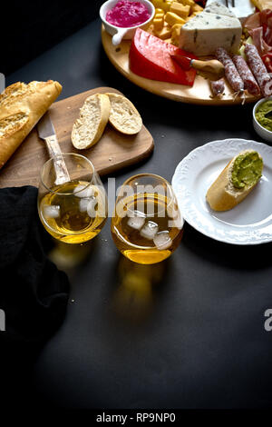 Conseil d'Antipasti avec différents en-cas du fromage et de la viande avec le vin blanc et baguette sur planche de bois sur tableau noir Banque D'Images