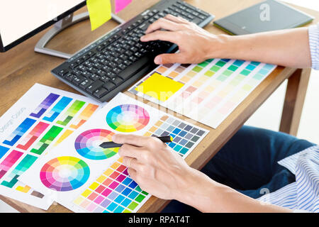 Designer graphique ou creative holding de la souris et faire son travail matériel couleur pantone swatch art échantillons tools at desk in office Banque D'Images