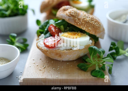 Sandwiches bagel au fromage à la crème, Avocat, tomates, œuf et verts sur fond de bois gris. Focus sélectif. La saine alimentation ou la nourriture végétarienne co Banque D'Images