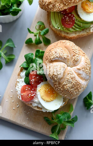 Sandwiches bagel au fromage à la crème, Avocat, tomates, œuf et verts sur fond de bois gris. Focus sélectif. La saine alimentation ou la nourriture végétarienne co Banque D'Images