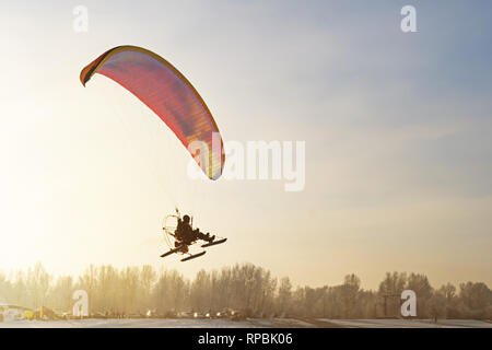 Un parapente vole au-dessus de la cime des arbres couverts de neige. Sur un vol en parapente motorisé de l'hiver, Banque D'Images