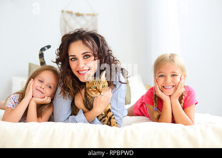 Heureux d'une mère et de deux de ses filles smiling câlins au lit. Famille heureuse à la maison avec le chat d'intérieur Banque D'Images