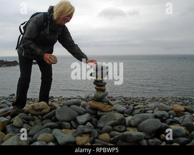 Femme blonde randonneur la construction d'un cairn de pierre à partir de galets sur Fontenelle Bay sur le sentier du littoral sur Guernesey dans les îles Anglo-Normandes.UK. Banque D'Images