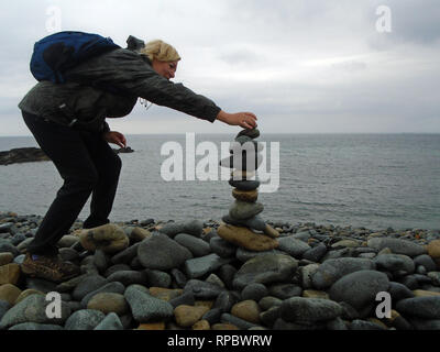 Femme blonde randonneur la construction d'un cairn de pierre à partir de galets sur Fontenelle Bay sur le sentier du littoral sur Guernesey dans les îles Anglo-Normandes.UK. Banque D'Images