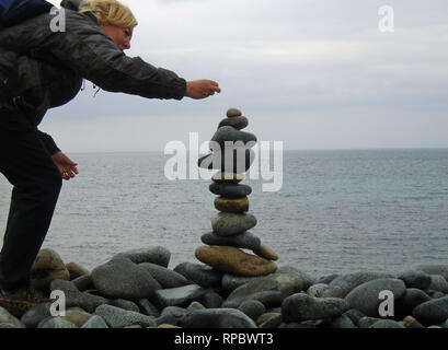 Femme blonde randonneur la construction d'un cairn de pierre à partir de galets sur Fontenelle Bay sur le sentier du littoral sur Guernesey dans les îles Anglo-Normandes.UK. Banque D'Images