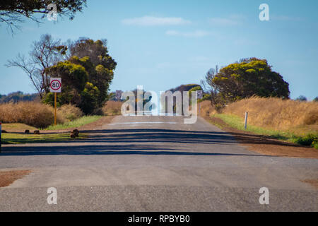 Route droite sans fin dans l'Outback australien avec soleil chaud provoquant Fata Morgana Banque D'Images