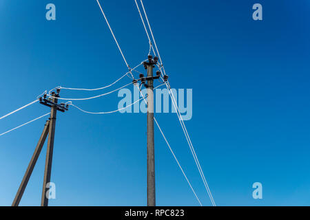 Deux poteaux de ligne électrique avec fils gelés en hiver, vu de l'angle faible contre le ciel bleu clair Banque D'Images