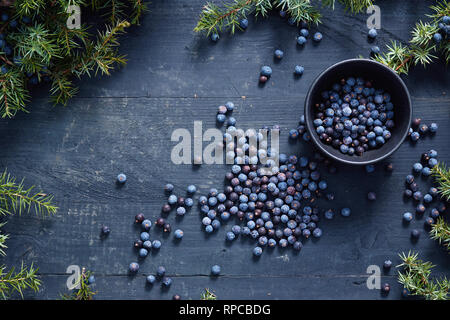 Les baies de genévrier sur et à côté de bol noir. Les baies de genévrier et les branches. Banque D'Images