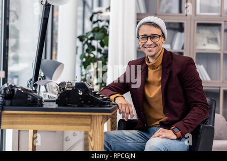 Bien-toiletté nifty smiling gentleman assis à un bureau avec des machines à écrire Banque D'Images