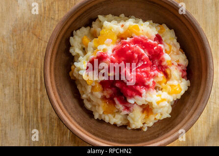 Vue de dessus sur un bol de faïence avec riz blanc cuit dans le lait avec sultana, morceaux de citrouille et aromatisé avec du jus de framboises fraîches et de miel Banque D'Images